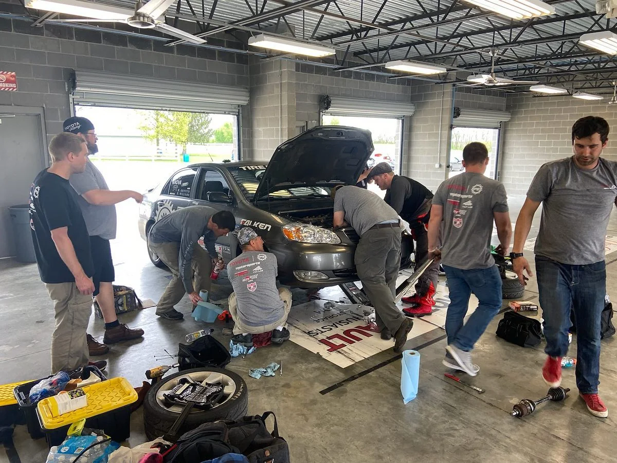 Dadbod Carmod crew working around a gray Corolla in a service bay