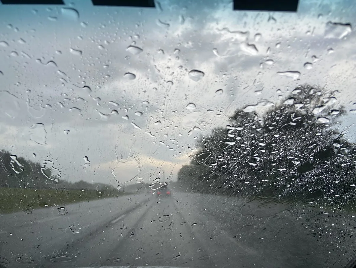 Rain-covered windshield view from inside a car during highway transit