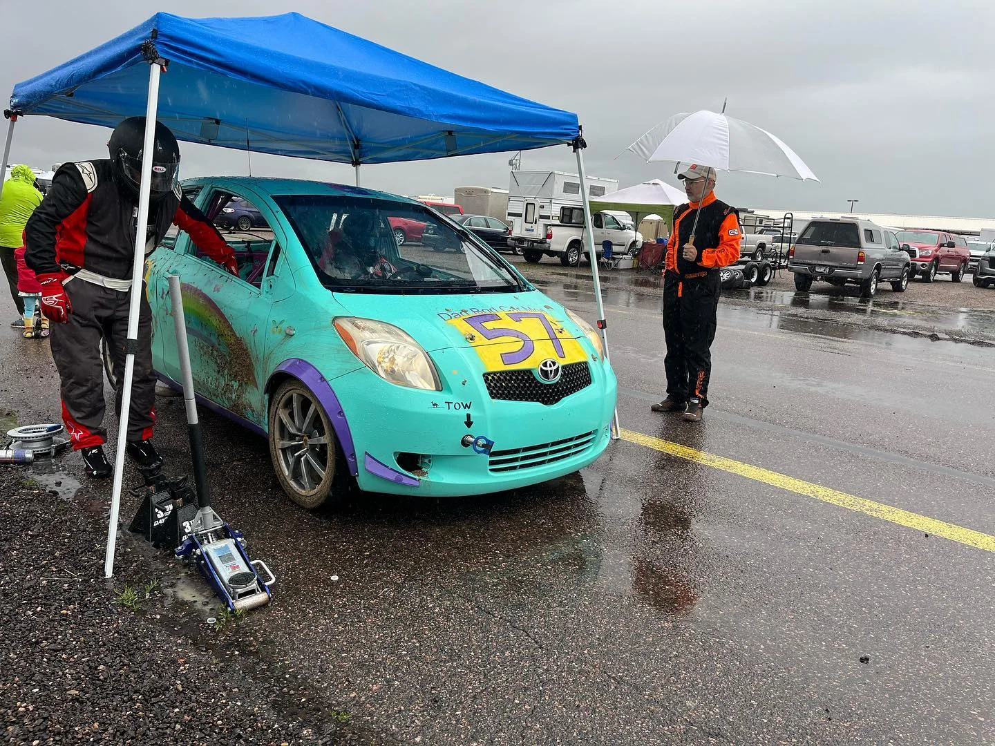 Turquoise number 57 Yaris being serviced under a canopy in a wet paddock